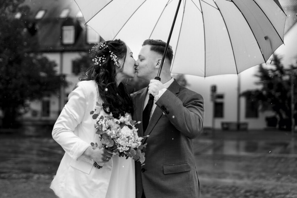 Brautpaar küsst sich unter Regenschirm nach Hochzeit im Standesamt