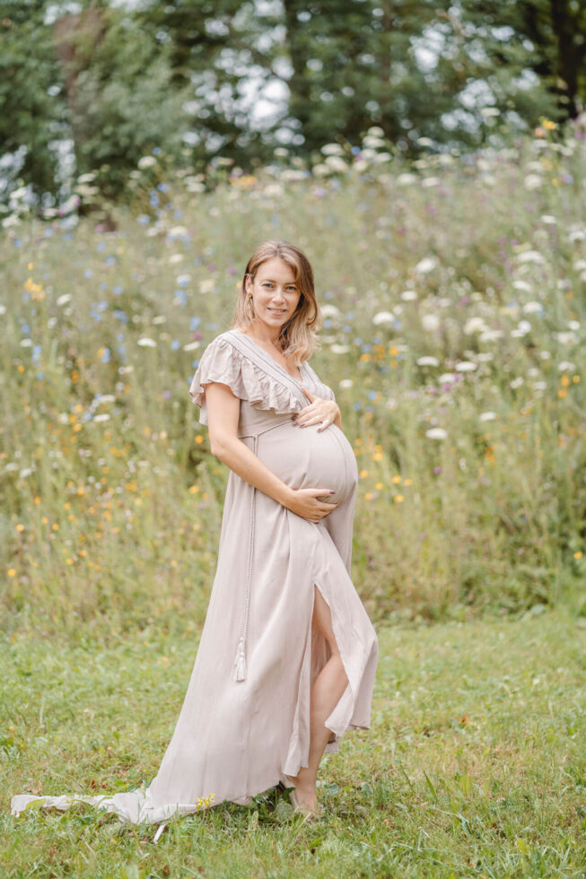 Bild von einem Babybauch Shooting bei dem die Schwangere ihren Bauch hält und in die Kamera blickt