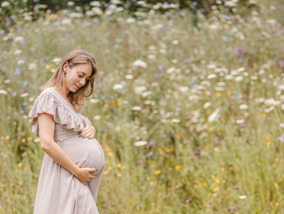 Schwangere auf Blumenwiese streichelt verträumt ihren Babybauch