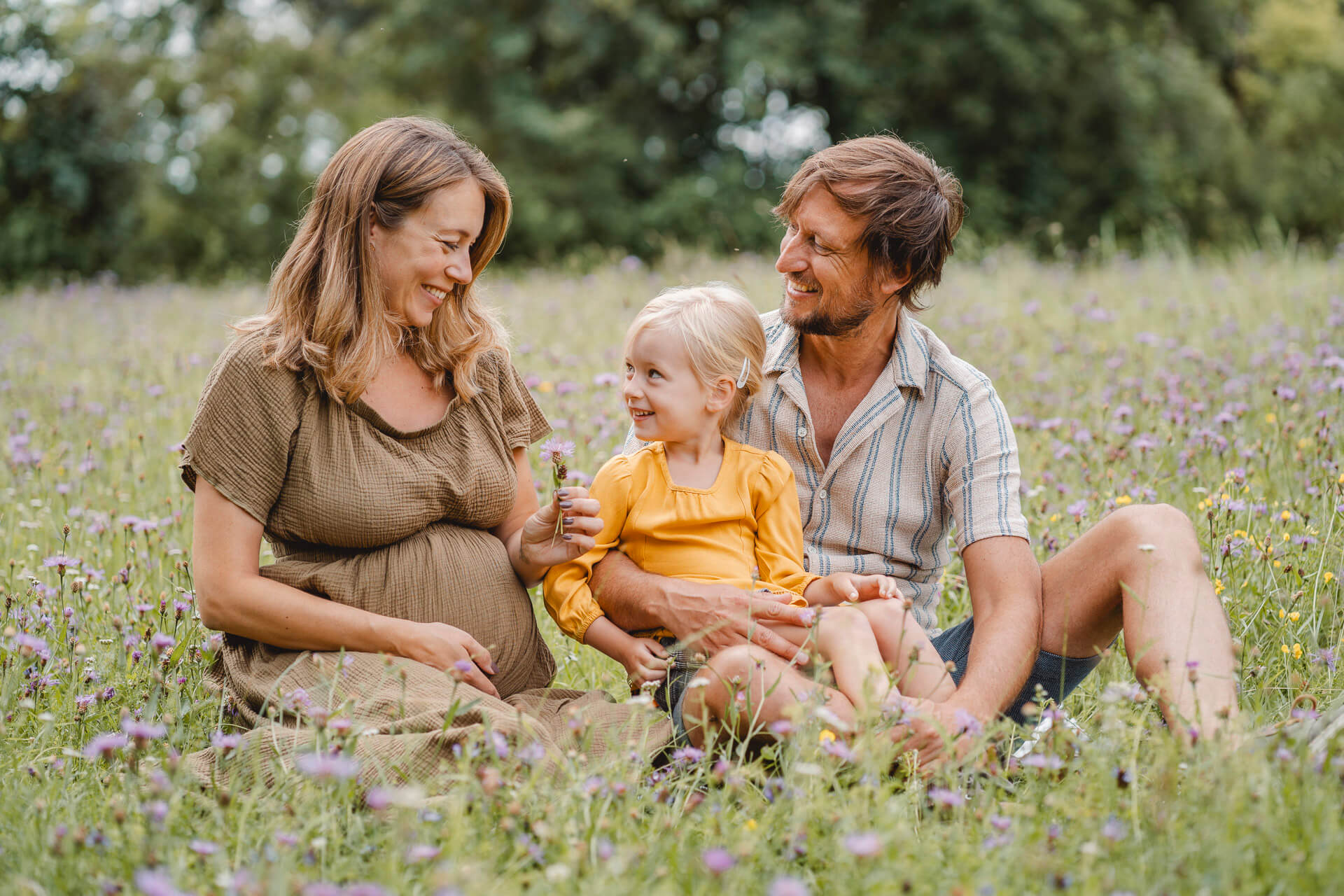 Bild einer Familie, die in einer Blumenwiese sitzt