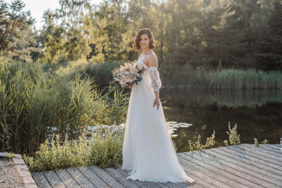 Hochzeitsfoto auf dem eine Braut auf einem Steg an einem See steht fotografiert von einer Hochzeitsfotografin in München