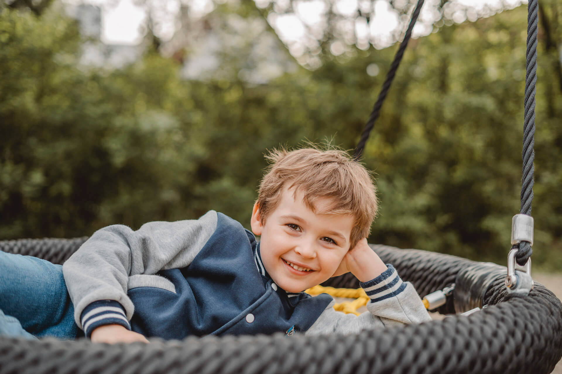 Kindergartenfotografie in München von einem Jungen, der lässig in einer Korbschaukel liegt