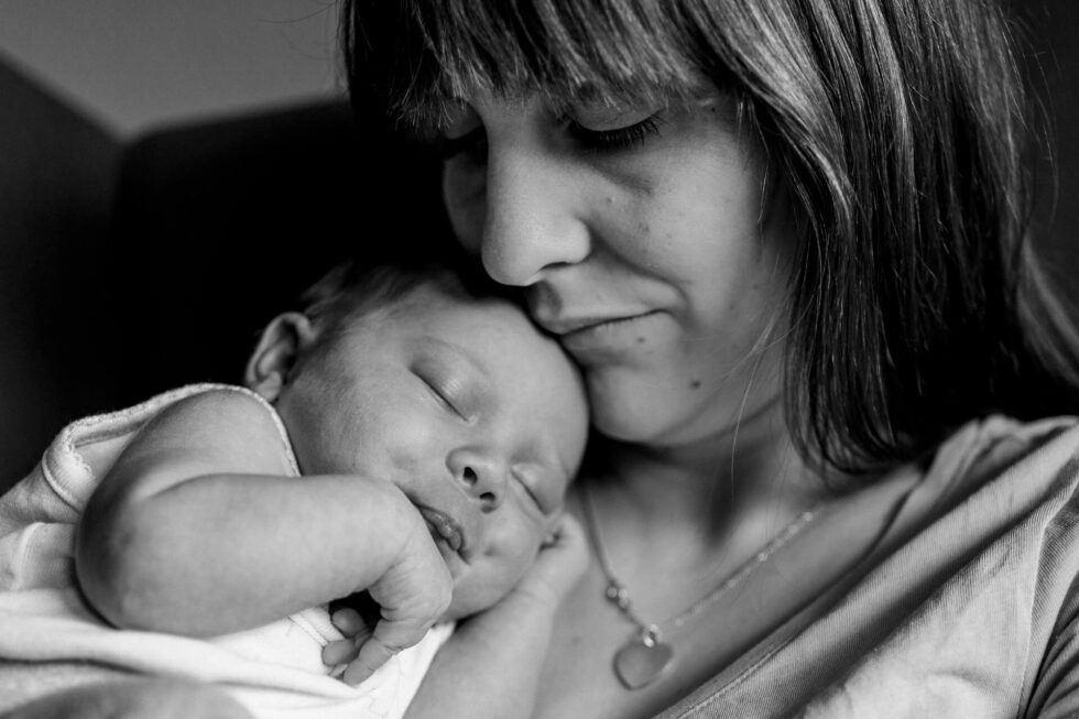 Baby schläft auf dem Oberkörper der Mutter liegend, fotografiert bei einem Neugeborenen Shooting in München